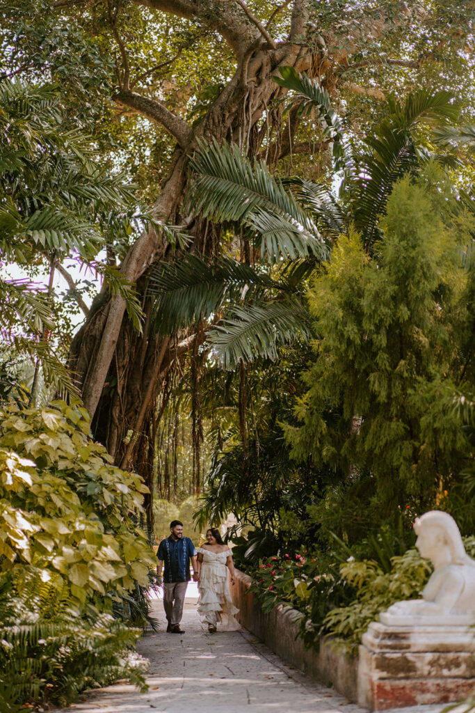 a couple walks hand in hand surrounded by giant trees at Vizcaya 