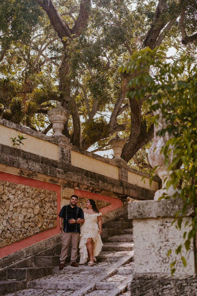 a girl looking at her fiance in front of trees at Vizcaya Museum in Miami