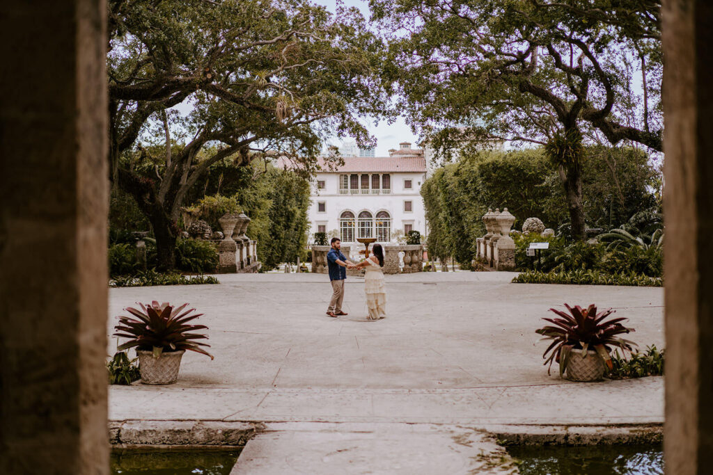 a couple hold hands while spinning with Vizcaya Museum behind them