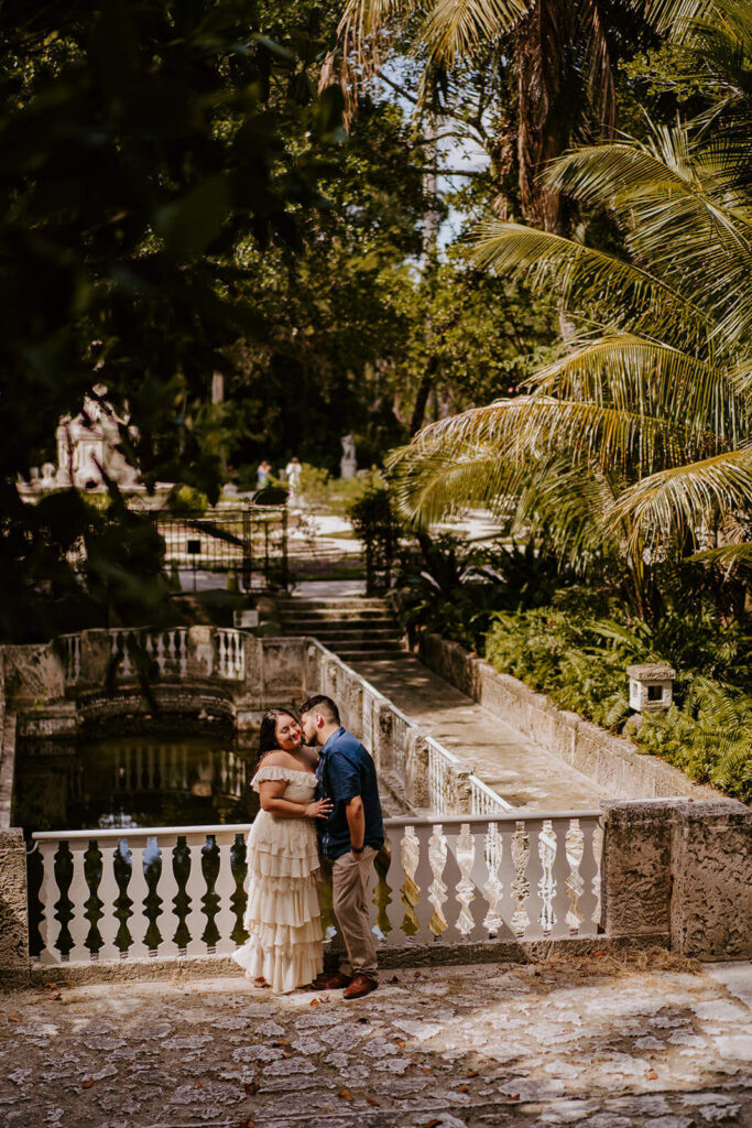 a man kisses his fiance in front of the beautiful architecture in the gardens of Vizcaya