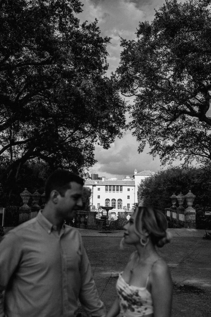 a couple looks at each other while Vizcaya Museum and Gardens shines bright in the distance