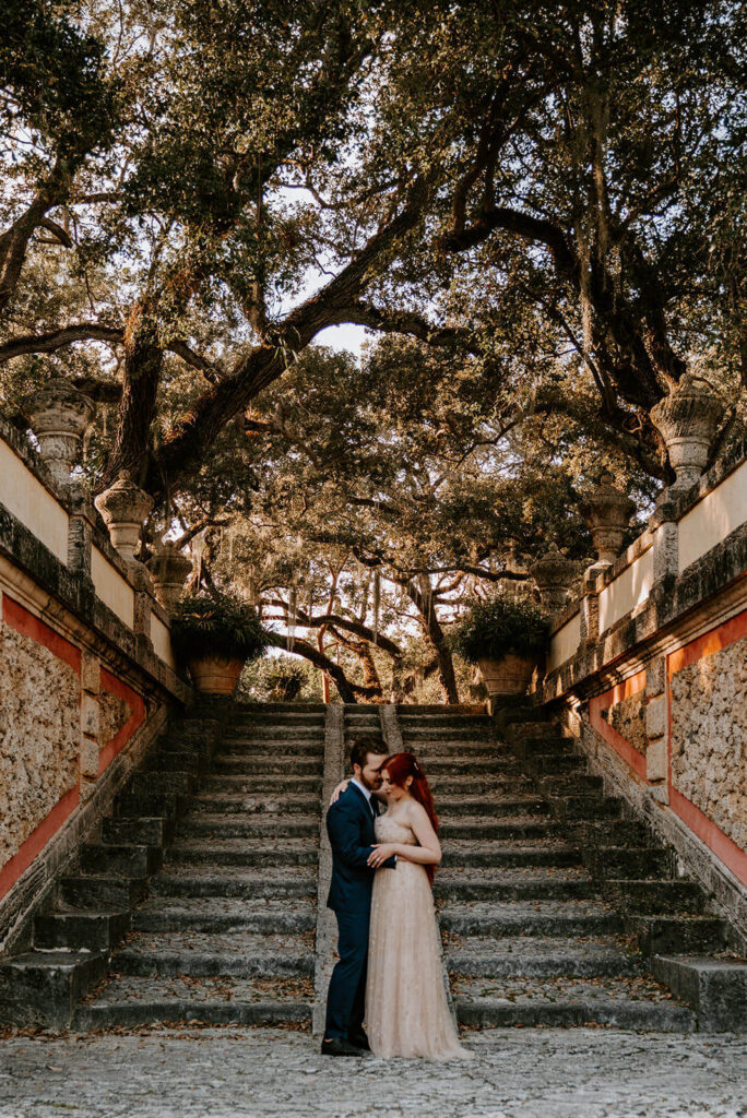 a couple poses in front of a staircase in the gardens of Vizcaya at sunset