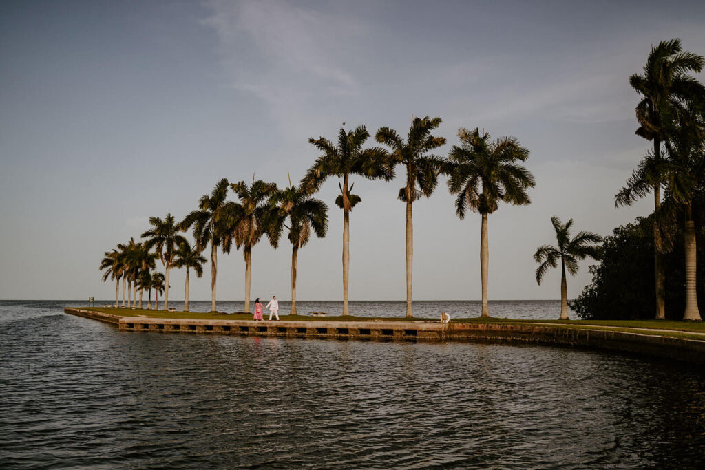 a bride and groom walk with giant palms surrounding them and ocean water all around in Miami