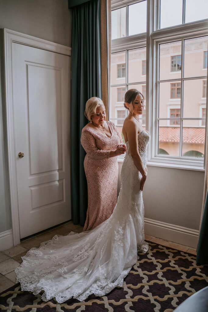 a mom helps her daughter put on her dress before her luxury wedding day