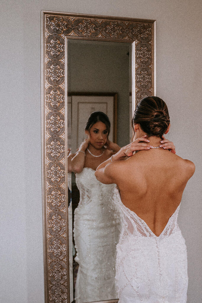a bride fixes her necklace in the mirror at her Biltmore Hotel wedding venue
