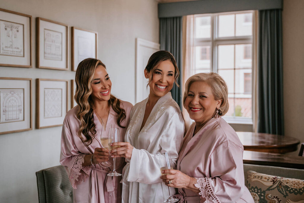a bride and her mom and sister laugh as they get ready for the wedding day at their luxury wedding venye