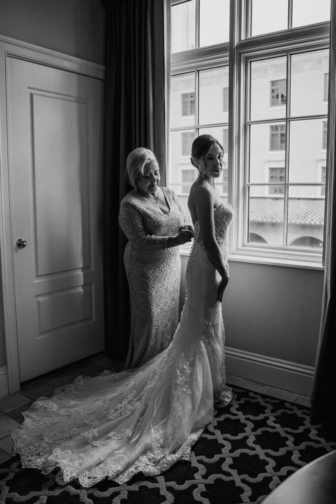 a mom helps her daughter put on her  wedding dress at their luxury miami wedding venue