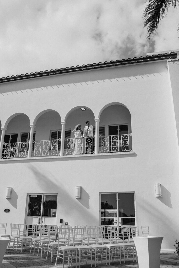 a bride and groom stand on a balcony overlooking their luxury miami wedding ceremony space