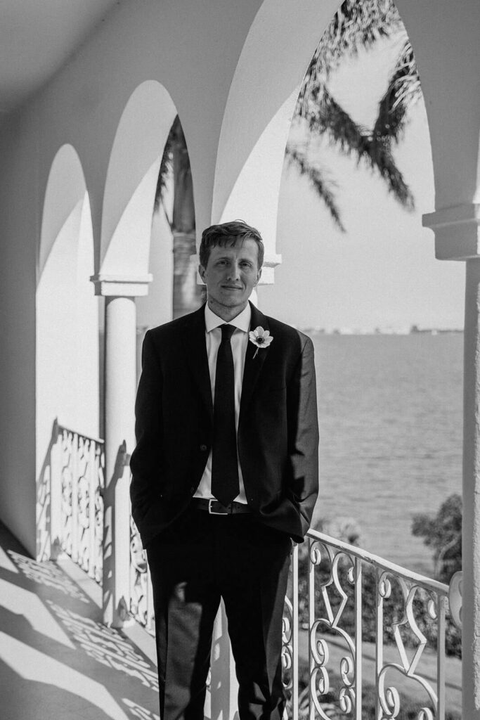 a black and white photo of a groom posing for a photo while the ocean is behind him