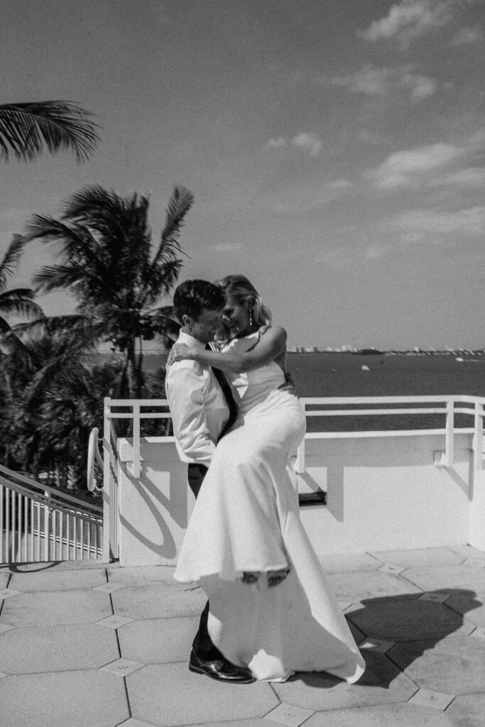 a groom picks up his bride on a balcony overlooking the ocean at their spring wedding