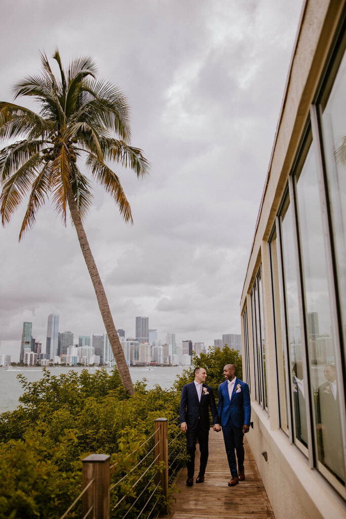 two grooms holding hands at the Rusty Pelican in Miami florida with the miami skyline behind them