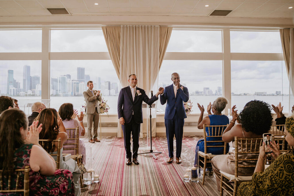 a couple crying as they are announced husband and husband on their wedding day with the miami skyline behind them