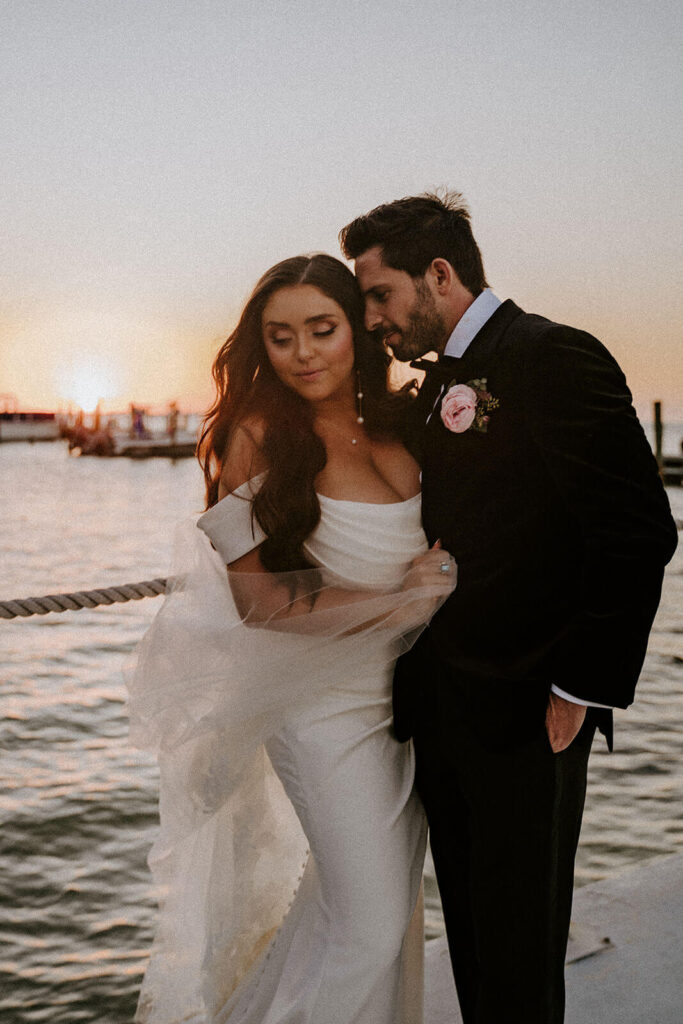 a groom cuddles up to his bride at golden hour overlooking the ocean at their wedding day at Bakers Cay Resort