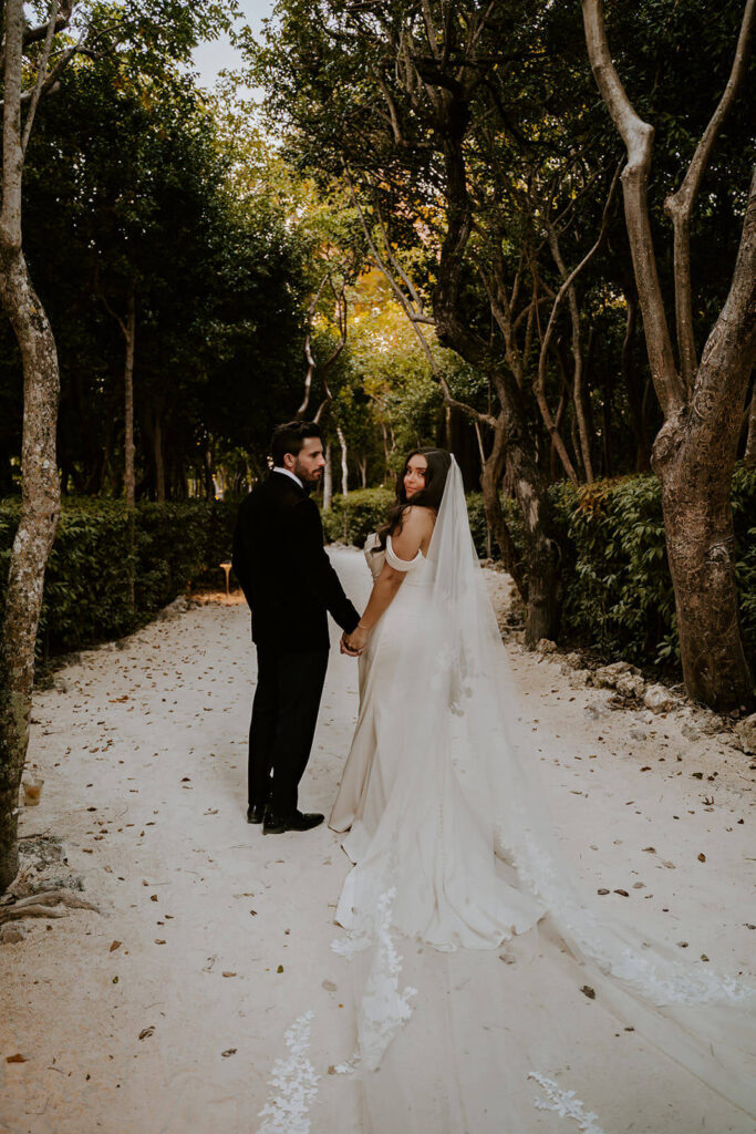 a couple walking away and looking at the camera surrounded by greenery at their Bakers Cay wedding
