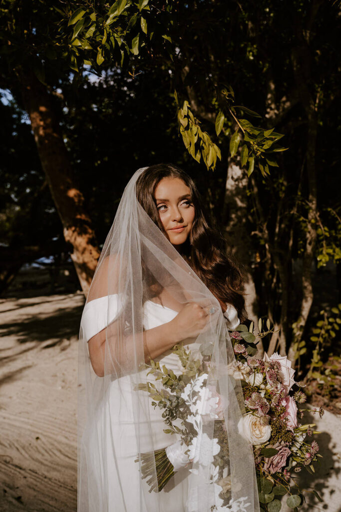 a bride poses with her veil in the sun on her wedding day