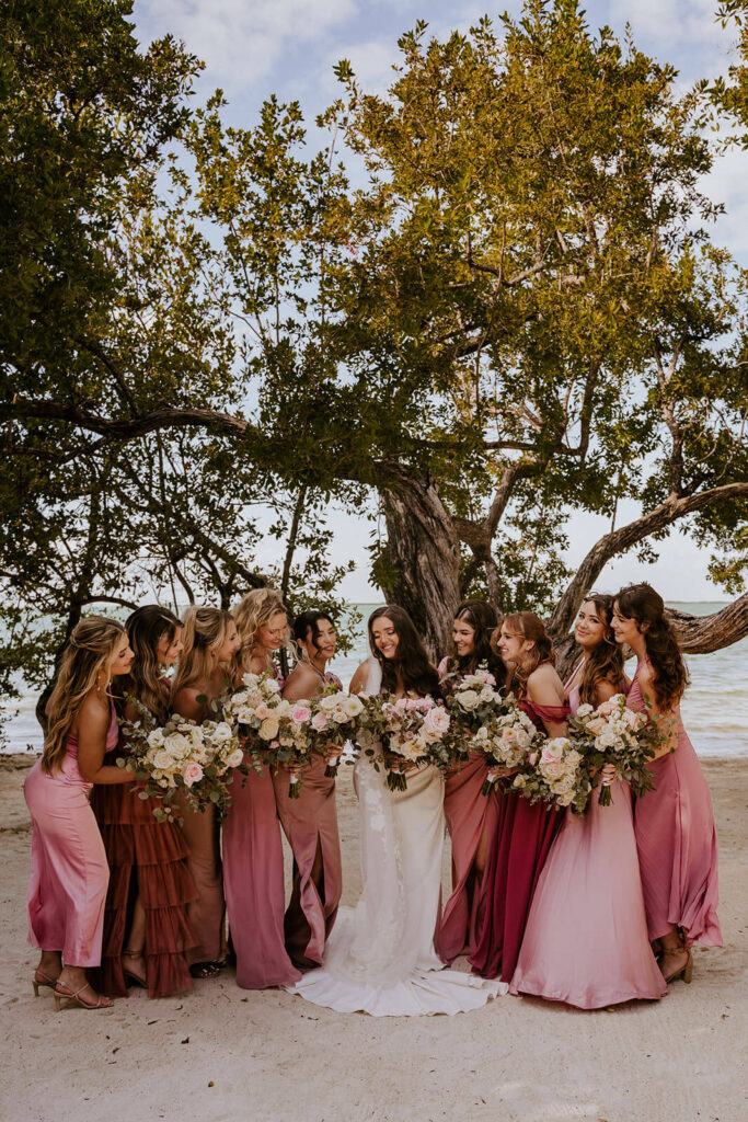 bridesmaids in pink posing with the bride in front of the palm trees and ocean in florida 