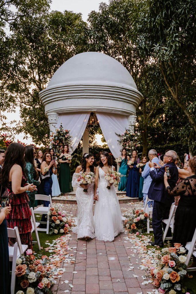 two brides walk happily away from their ceremony space after their wedding day in miami