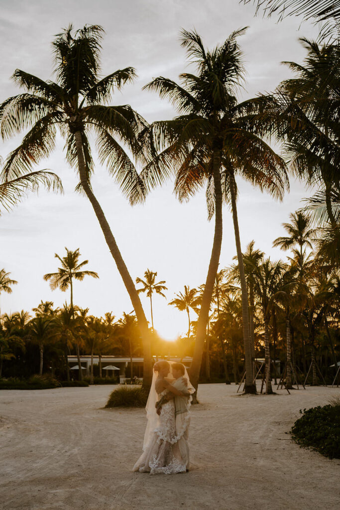 a couple hugging at golden hour in between two palm trees under the veil on their weding day