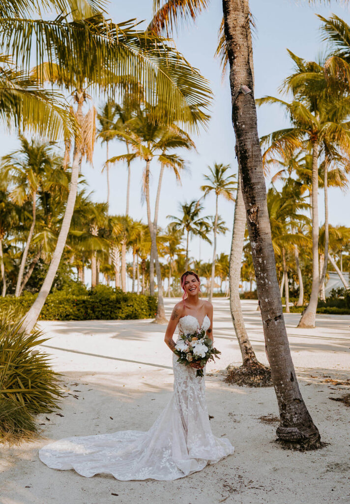 a bride laughs as she poses for a photo in florida surrounded by palm trees