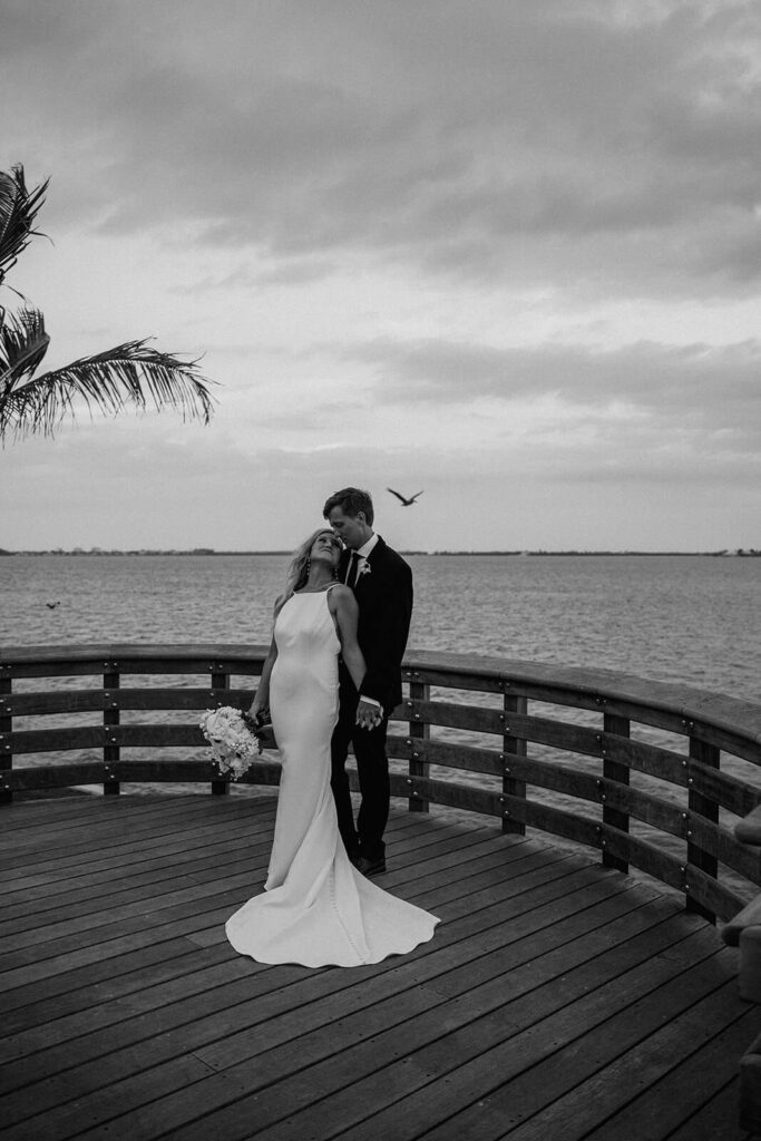a couple posing while holding hands on a walkway on their wedding day overlooking the ocean