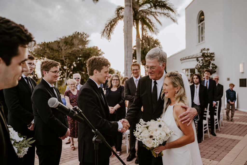 a father of the bride shaking the hand of the groom while he walks his daughter down the aisle on her wedding day