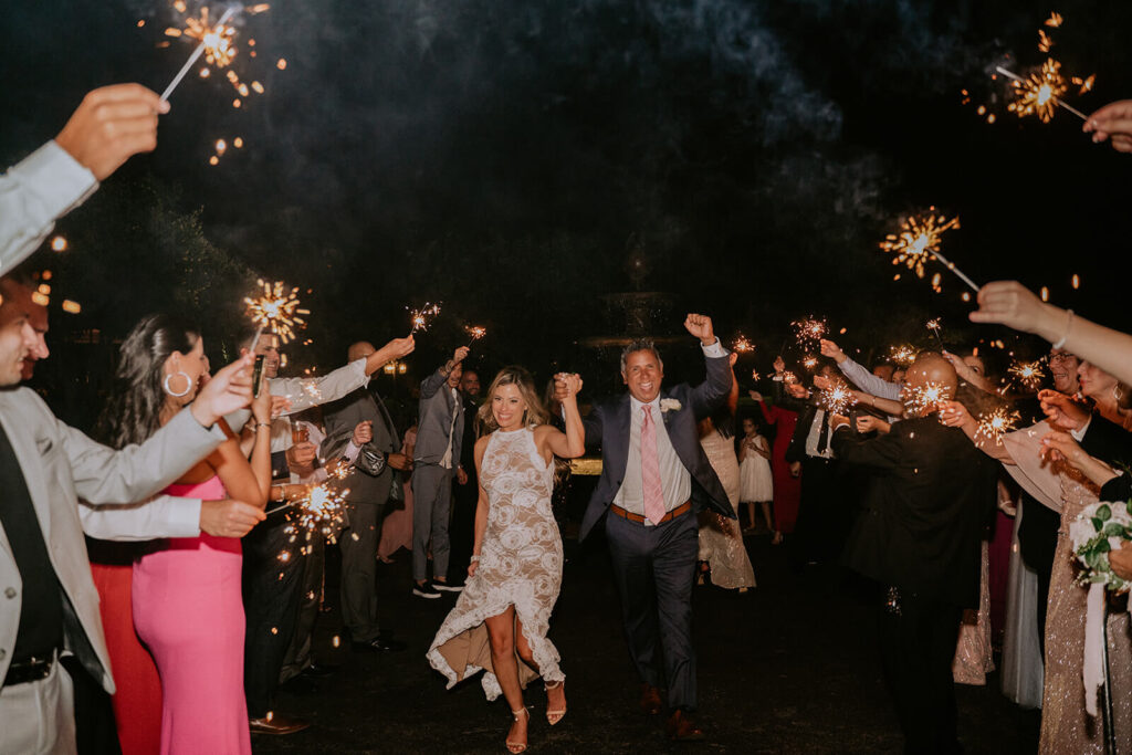 a couple runs through a line of their family and friends holding sparklers at the end of their wedding night in miami