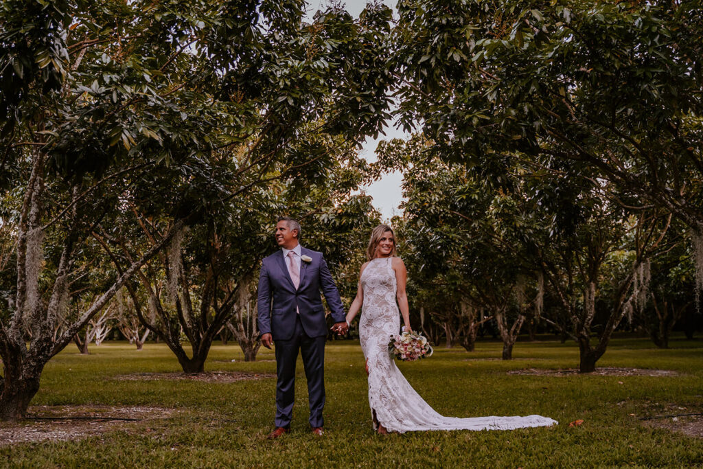 a couple poses while holding hands in the groves at longans place