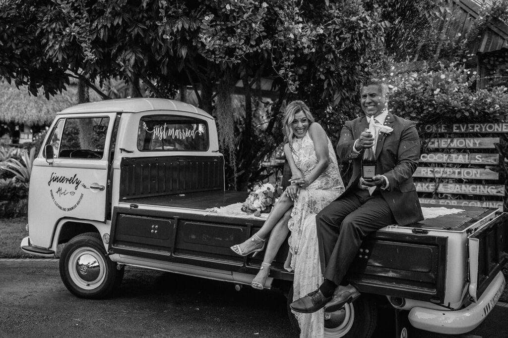 a couple pops a bottle of champagne while sitting on a truck at their wedding in miami