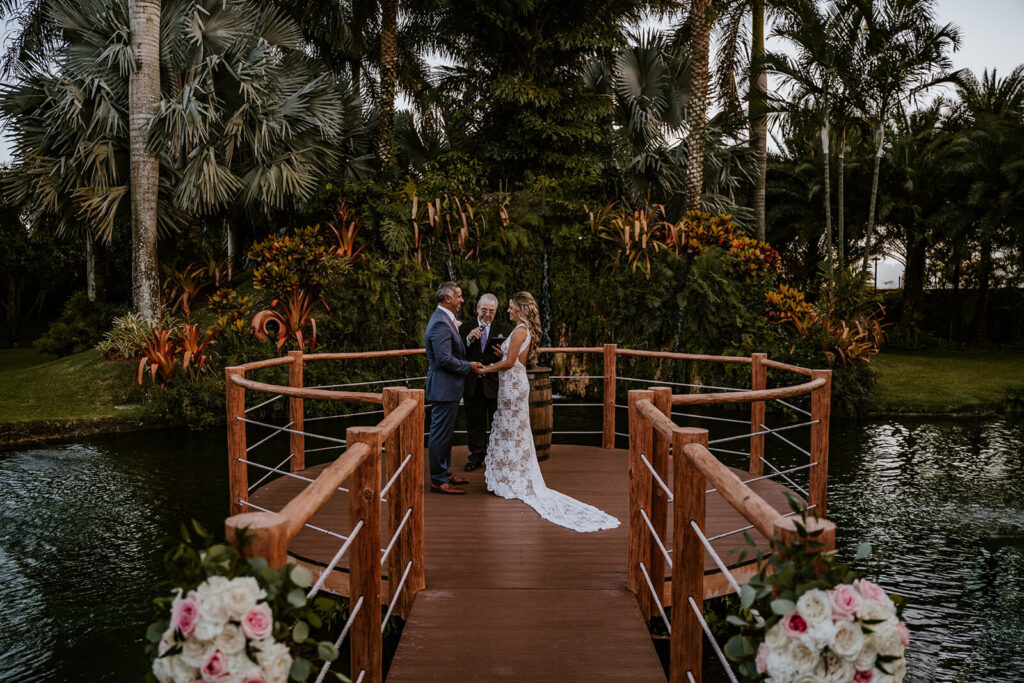 a couple holds hands at their ceremony location at the deck over the pond at their wedding venue in miami.