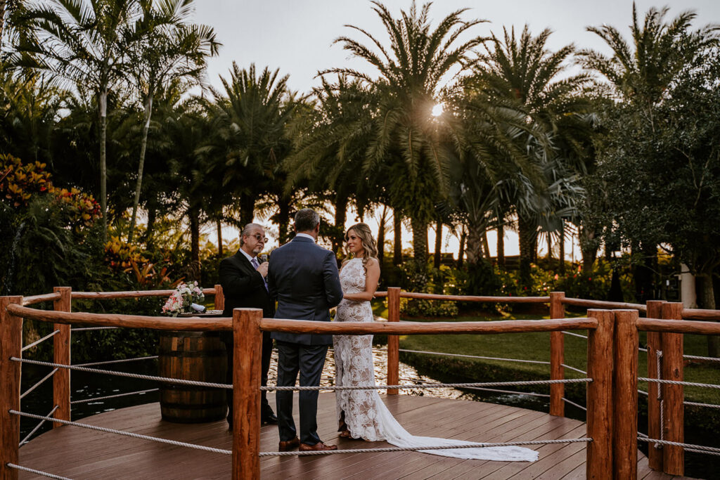 a bride and groom exchanging vows at their ceremony while the sun sets behind them at longans place