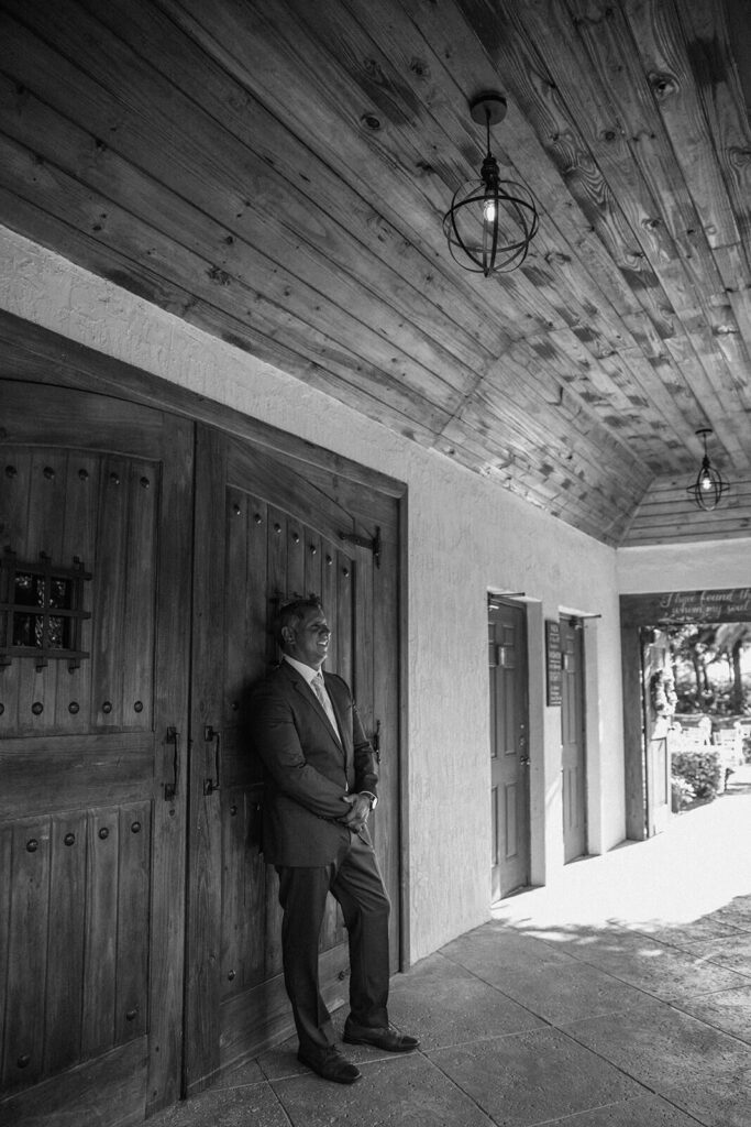 a groom leans on a wall at the main barn at longans place on his wedding day