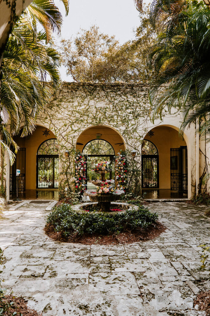 the courtyard of Villa Woodbine in Miami featuring a beautiful fountain covered with florals with 3 arches behind 