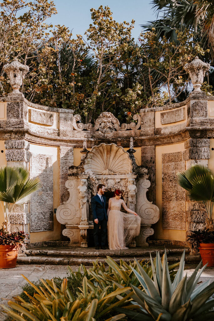 a couple poses for their wedding in front of a statue at Vizcaya Museum and Gardens