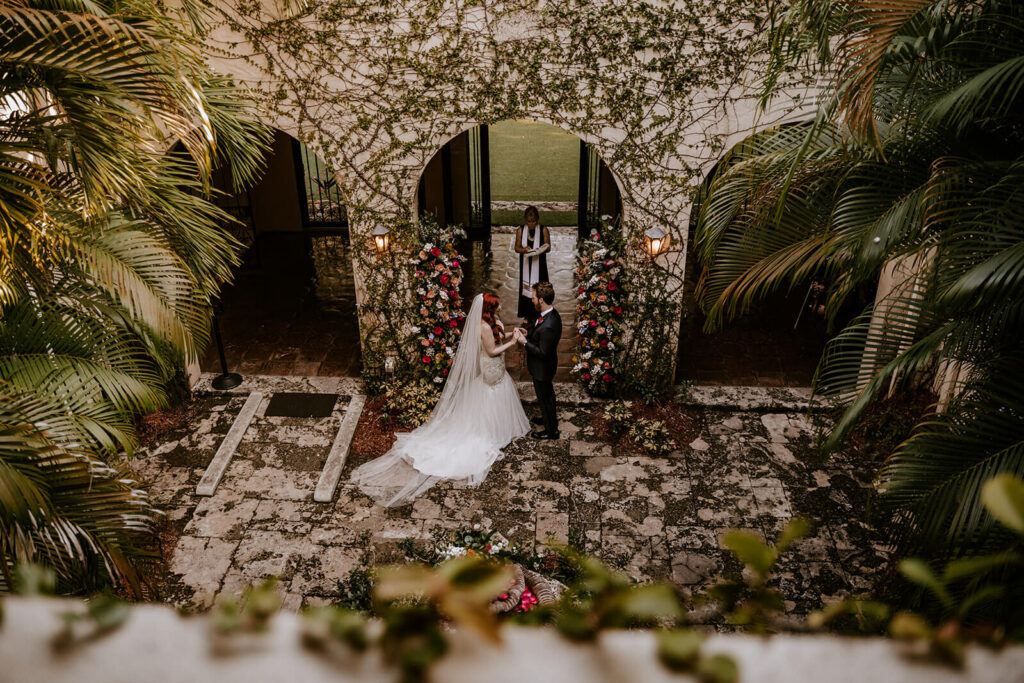 a couple holds hands at their ceremony while an officiant marries them surrounded by florals 