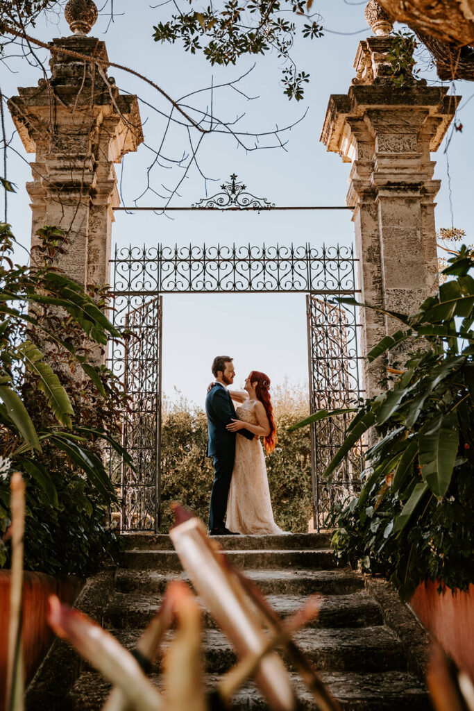 a bride and groom pose under a gate at Vizcaya in Miami florida on their wedding day