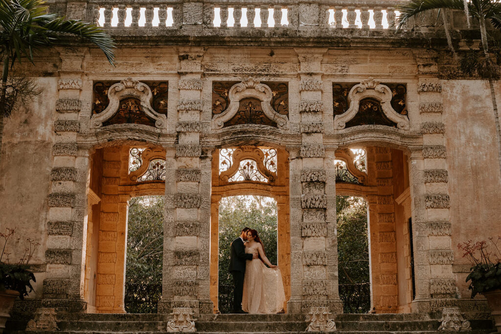a couple poses with the bride holding the train of her dress in the middle arch at Vizcaya