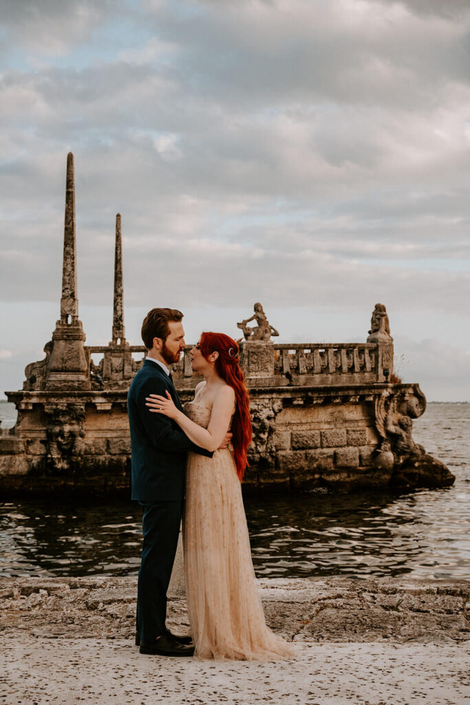 a couple hugs in front of a structure in the water at their miami wedding venue