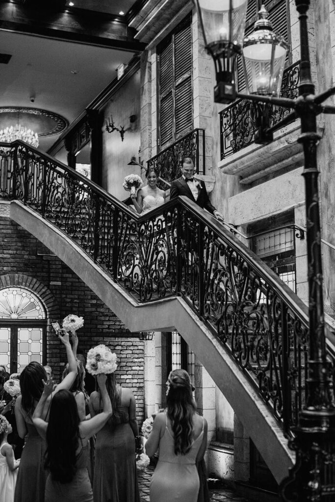 a couple makes their grand entrance as their wedding party cheers for them on the stairs at the Cruz Building in miami