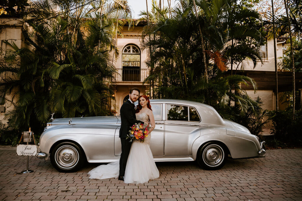 a couple posing with their car at Villa Woodbine in Coconut Grove, Miami on their wedding day