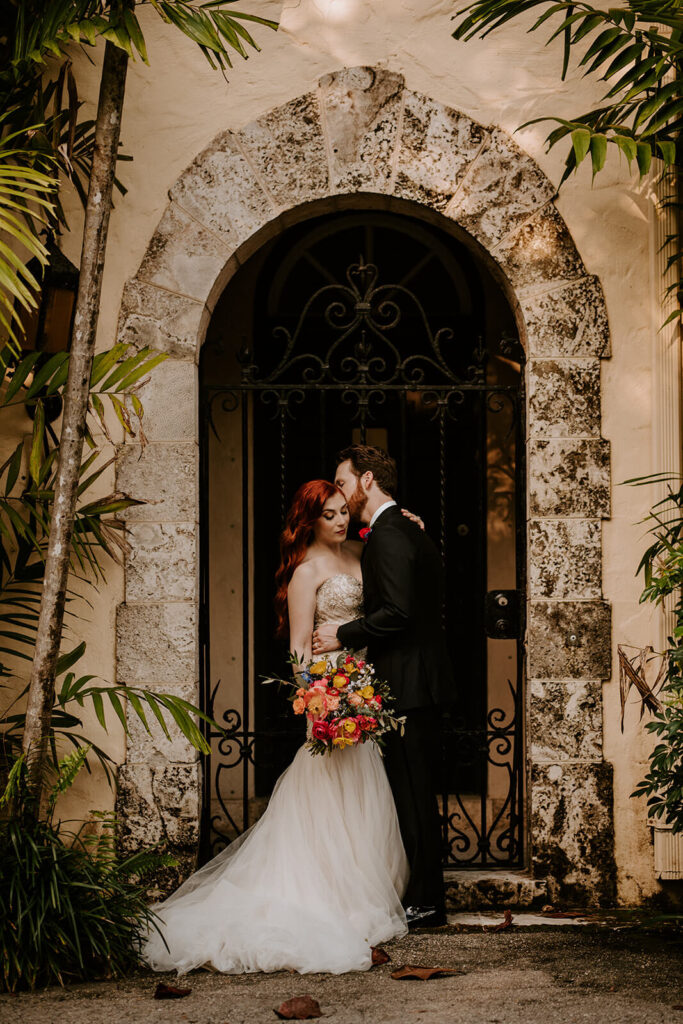 a groom kisses his bride on the cheek in an archway at their miami wedding venue