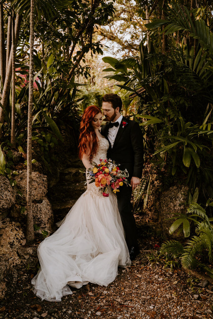 a bride with red hair and her groom pose for a photo around trees at Villa Woodbine in Miami