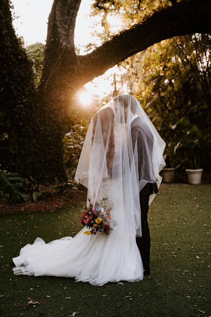 a couple kisses under their veil in front of the sunset at their Miami wedding venue Villa Woodbine