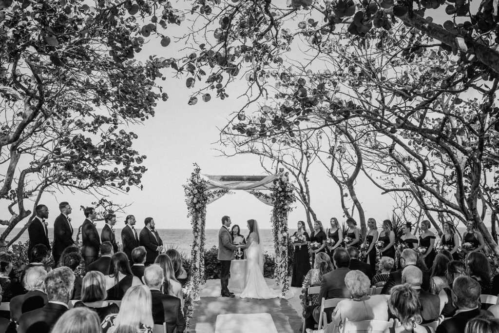a couple stands at their ceremony with their bridesmaids and groomsmen in front of the ocean at their miami wedding venue