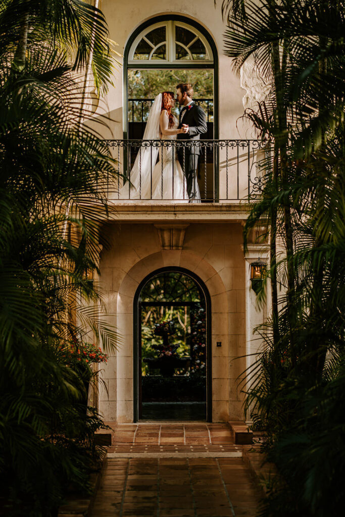 a couple poses outside on the balcony of their wedding venue