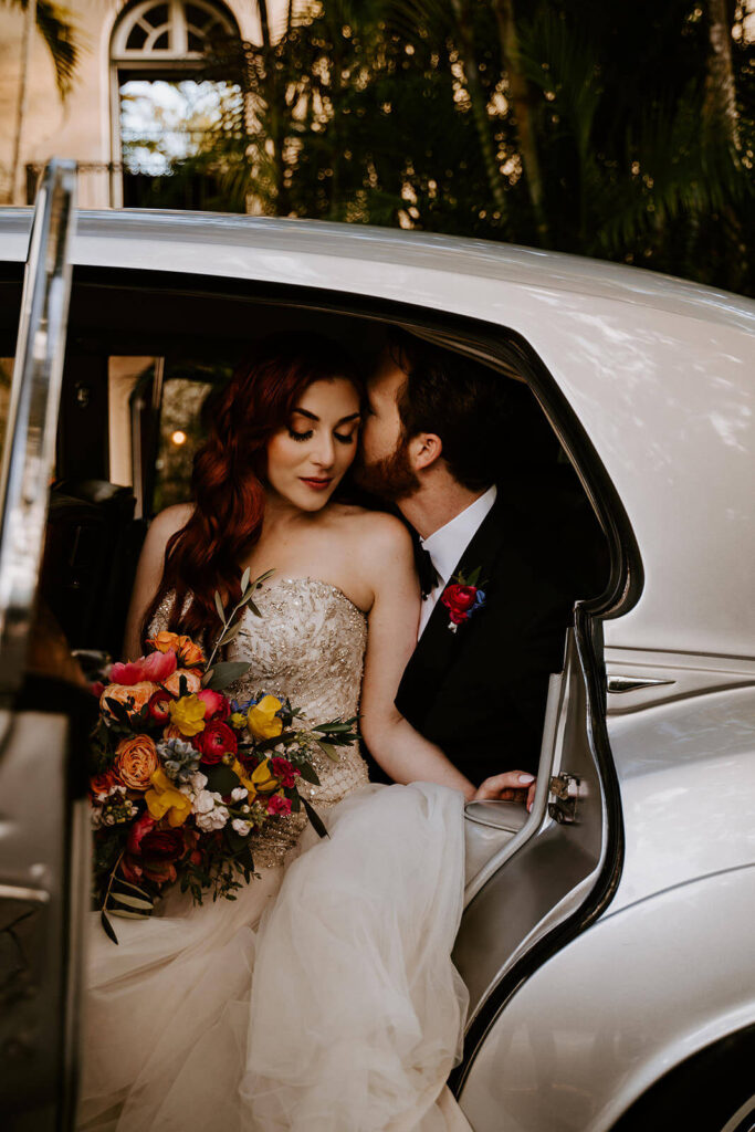 a couple poses in their car in front of their wedding venue