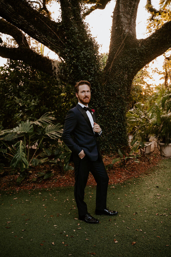 a groom poses for the camera in front of the tree at Villa Woodbine