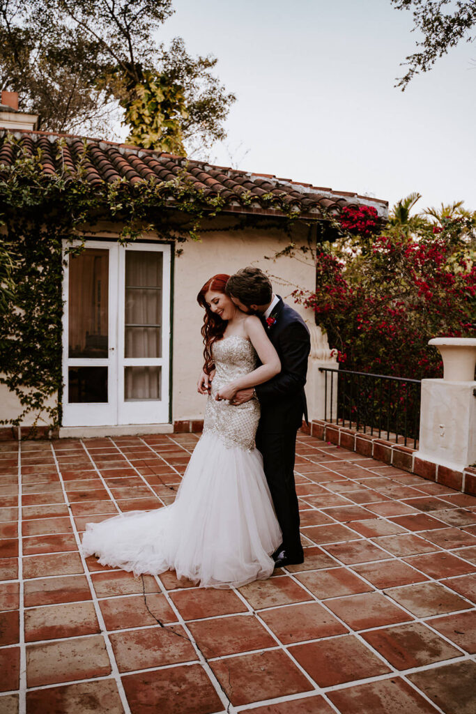 a groom hugs his bride from behind on the balcony at Villa Woodbine
