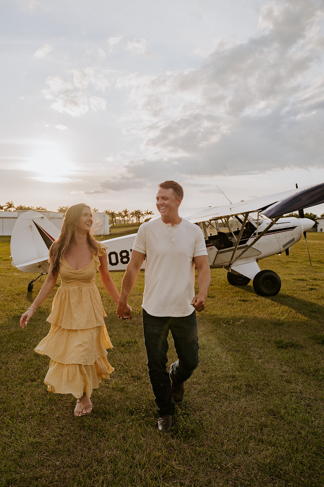 Man and woman hold hands in front of an airplane