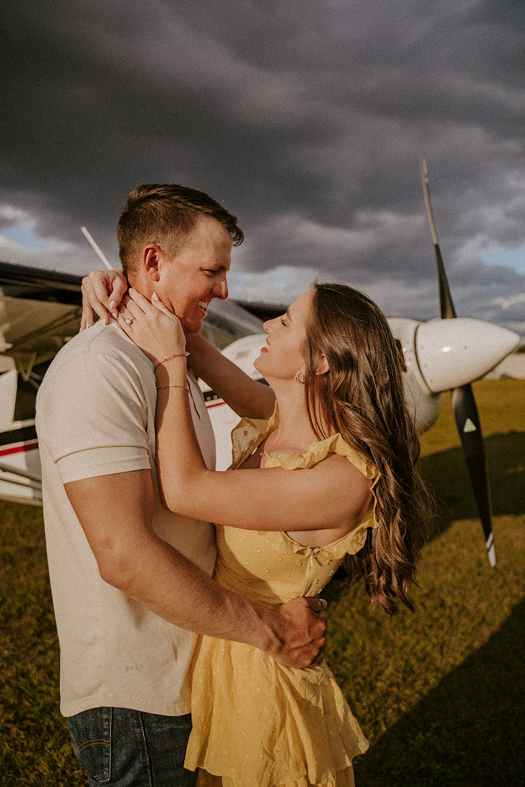 Man and woman embrace in front of an airplane during engagement photos