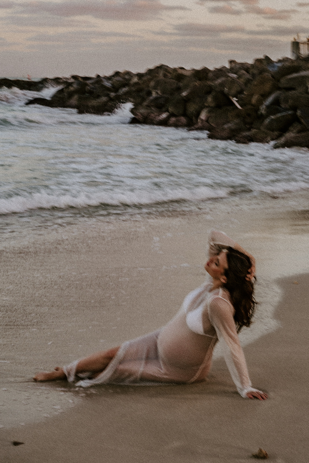 Woman sitting in sand at beach maternity photoshoot